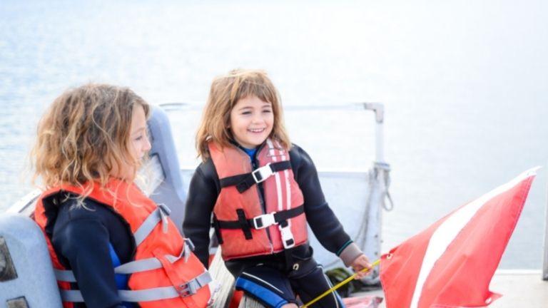 İki kız çocuğu teknede can yeleği giymiş bir şekilde yolculuk ediyor.