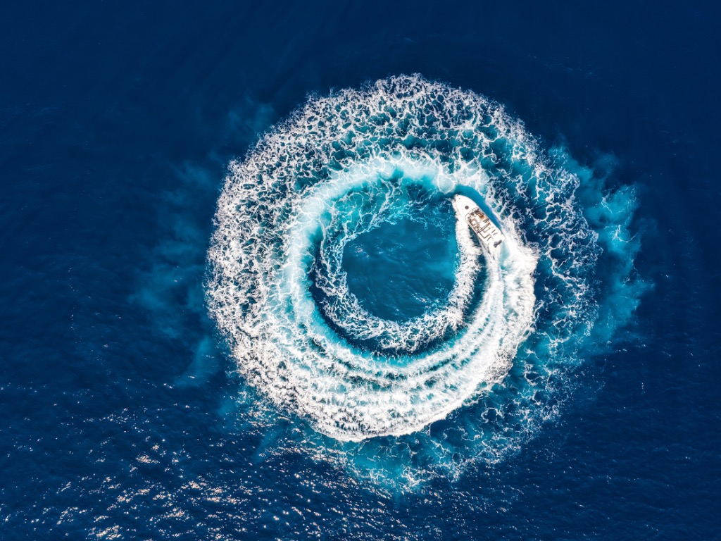 Motorlu tekne, motorlarıyla mavi denizin üzerinde bir dalga çemberi oluşturuyor ve köpürüyor
